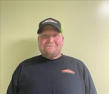 Man standing against a green wall with a Servpro shirt on