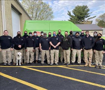 Group of men & women standing in uniforms and masks in front of Servpro trucks