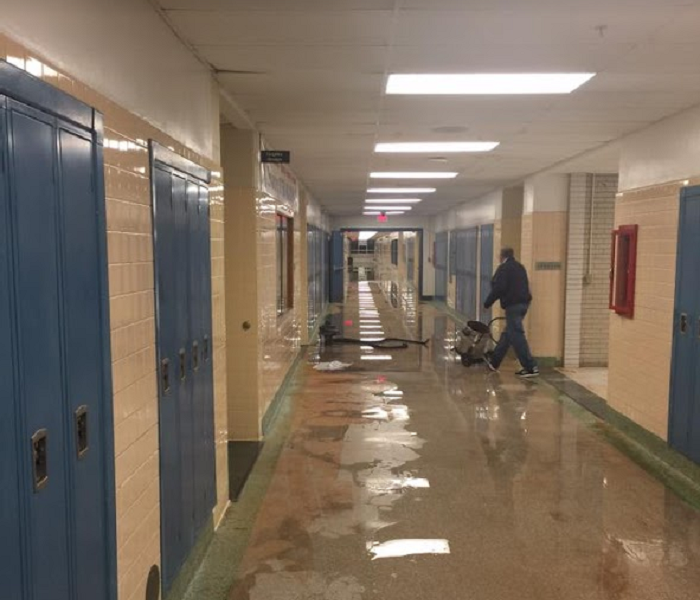 Man with water removal equipment in flooded school hallway